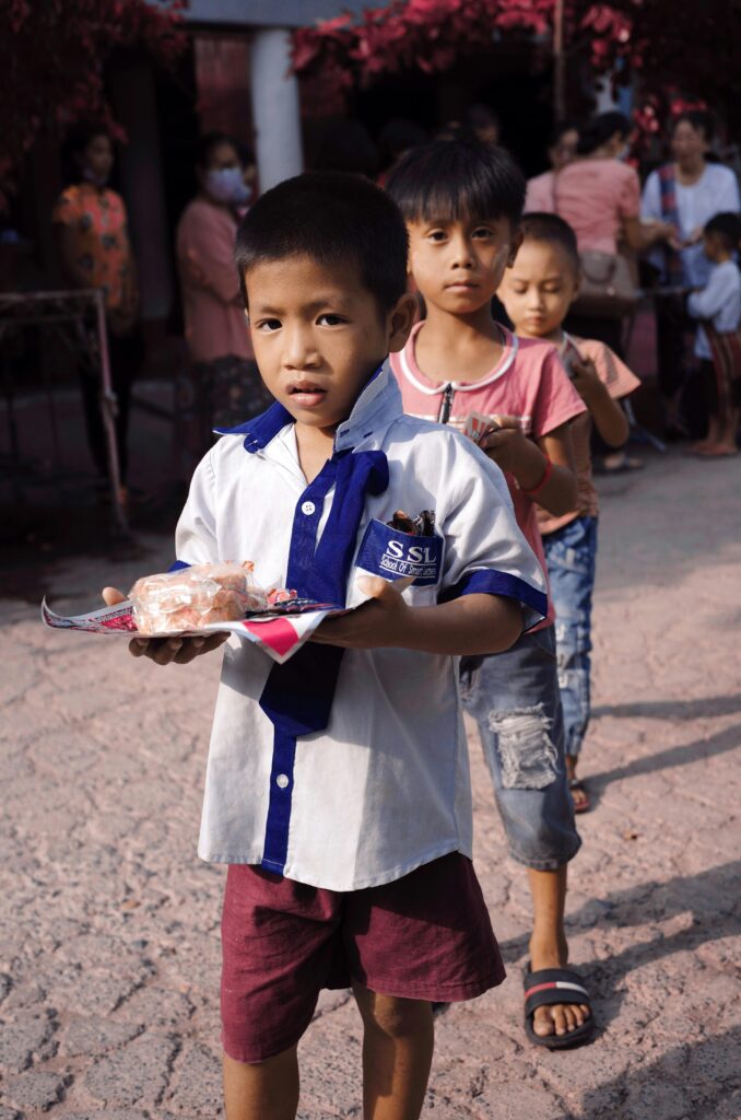 Young boys lined up outdoors in Mandalay to receive donations during a charity event.